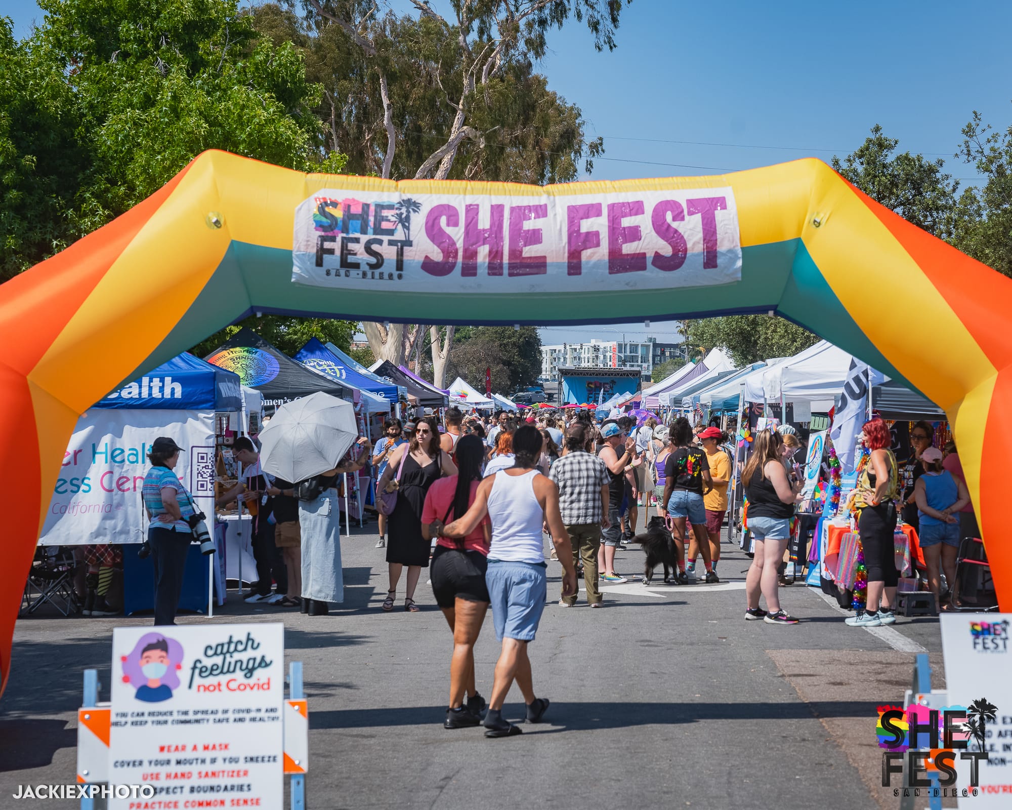 People walk under a large arch that says "She Fest" at a street fair event