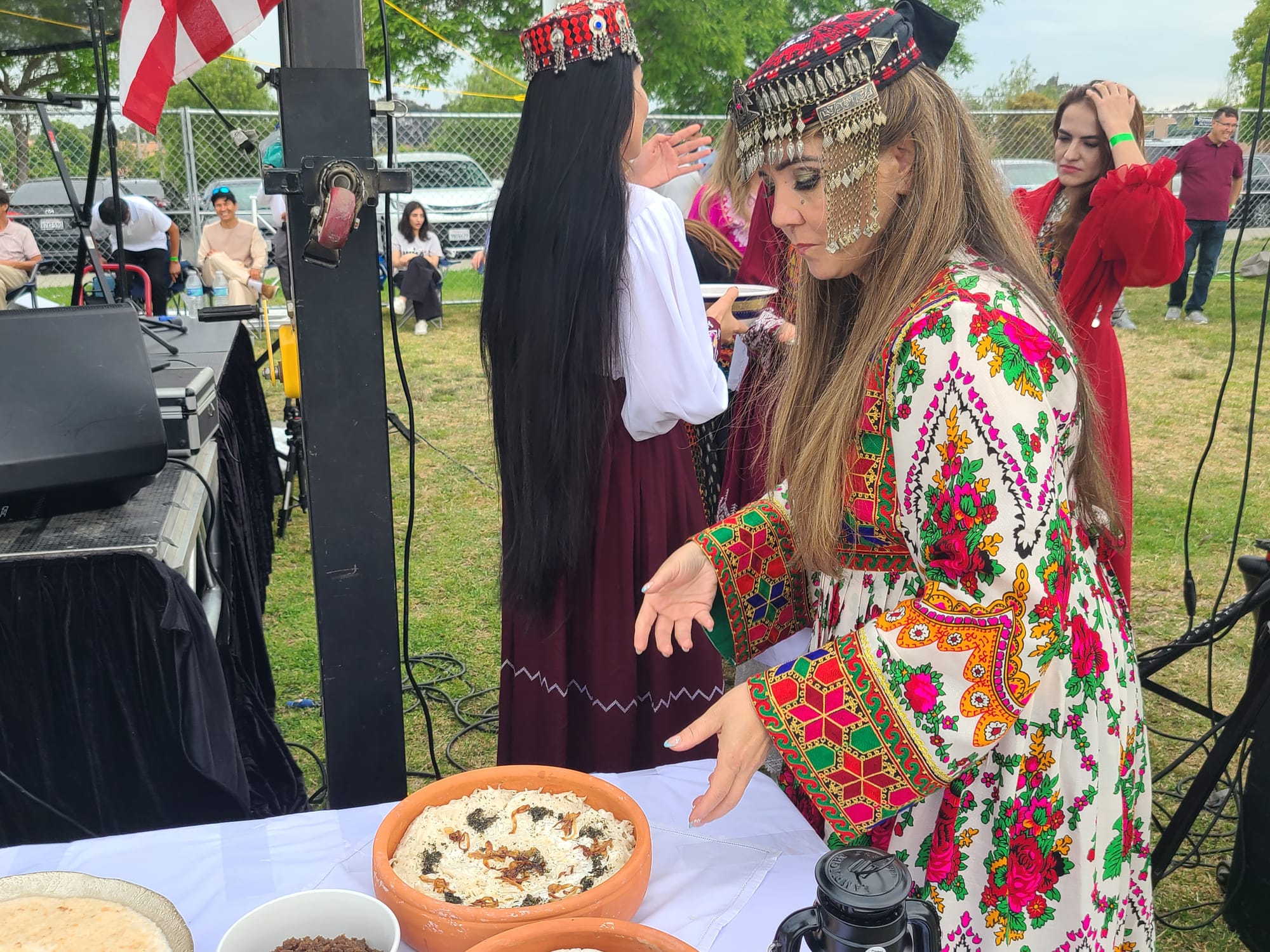 A woman in a colorful dress and hat bends forward to pick up a bowl of rice on a table