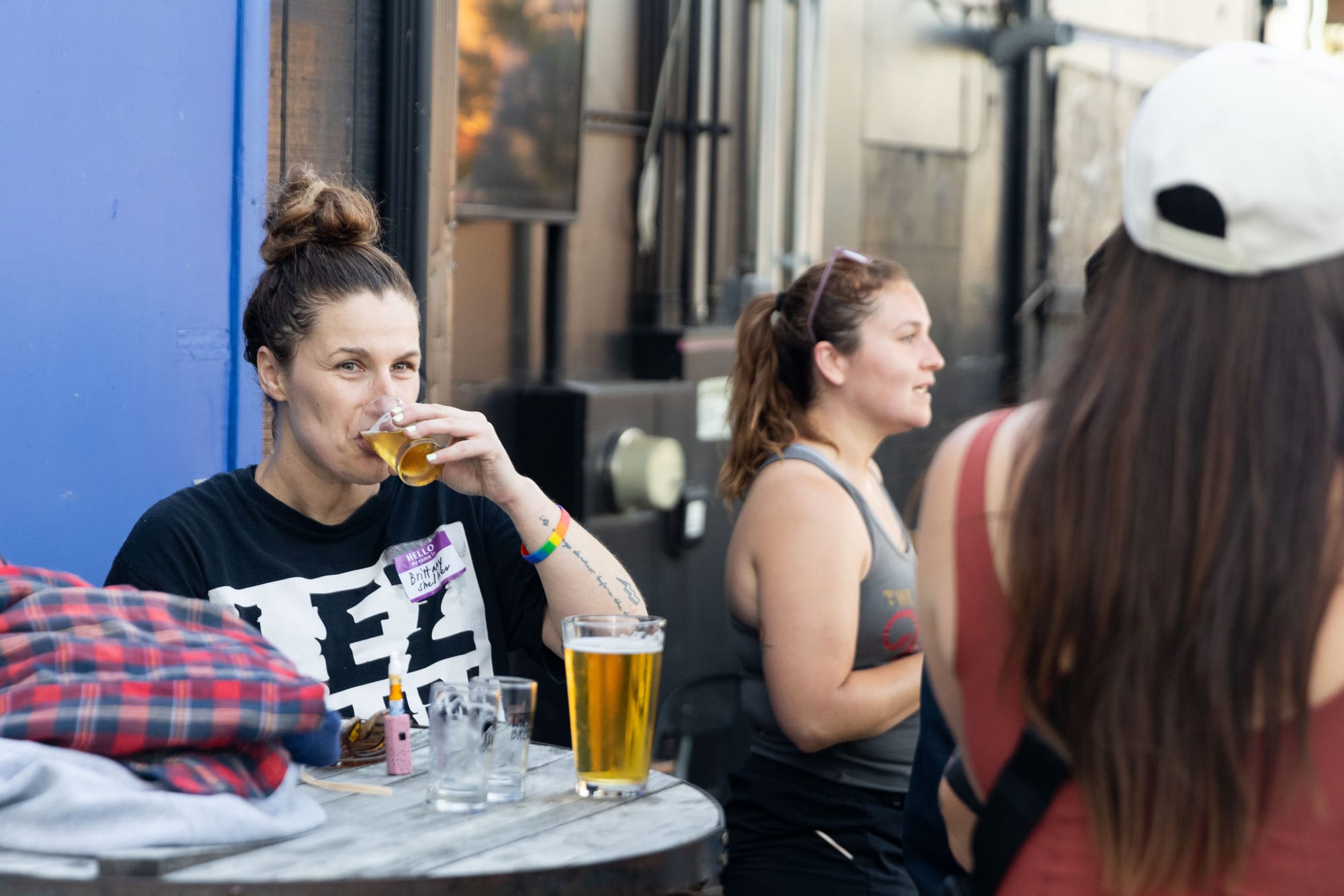 A person wearing a t-shirt that says "LEZ Run" drinks a small glass of beer next to other people