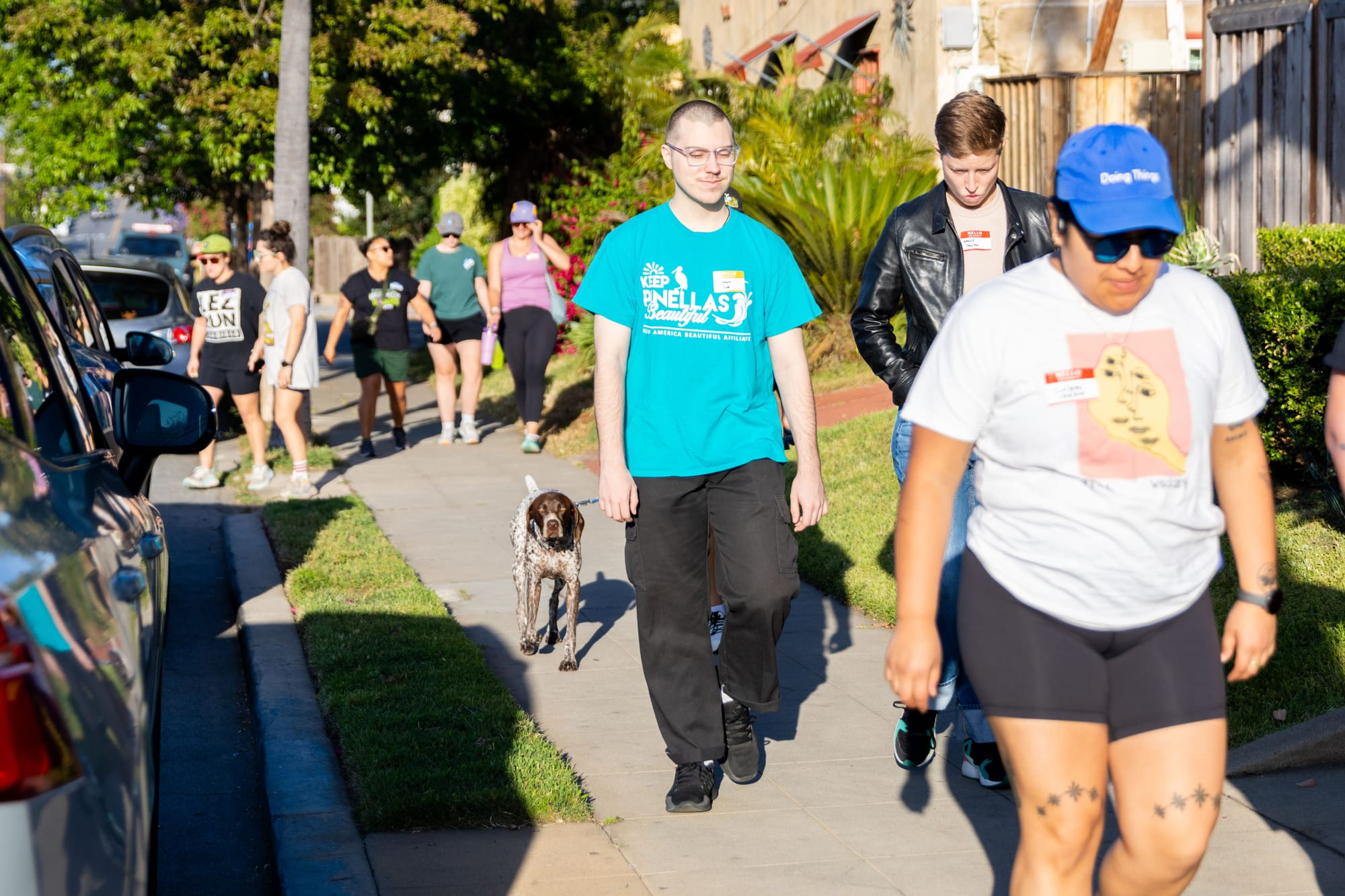 A group of people and a dog go for a walk down a city sidewalk