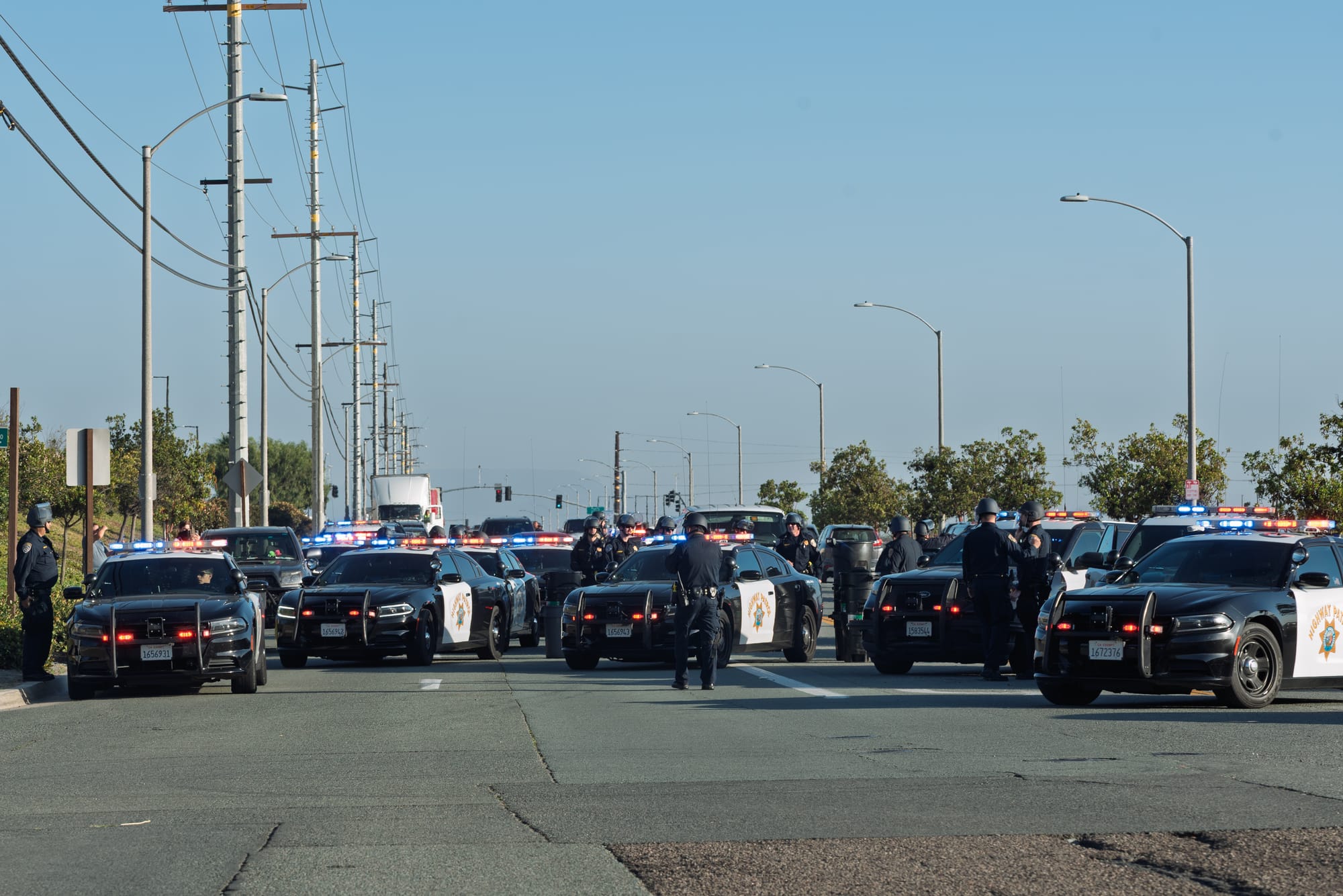 Police cars fill the street and officers in helmets stand by the cars