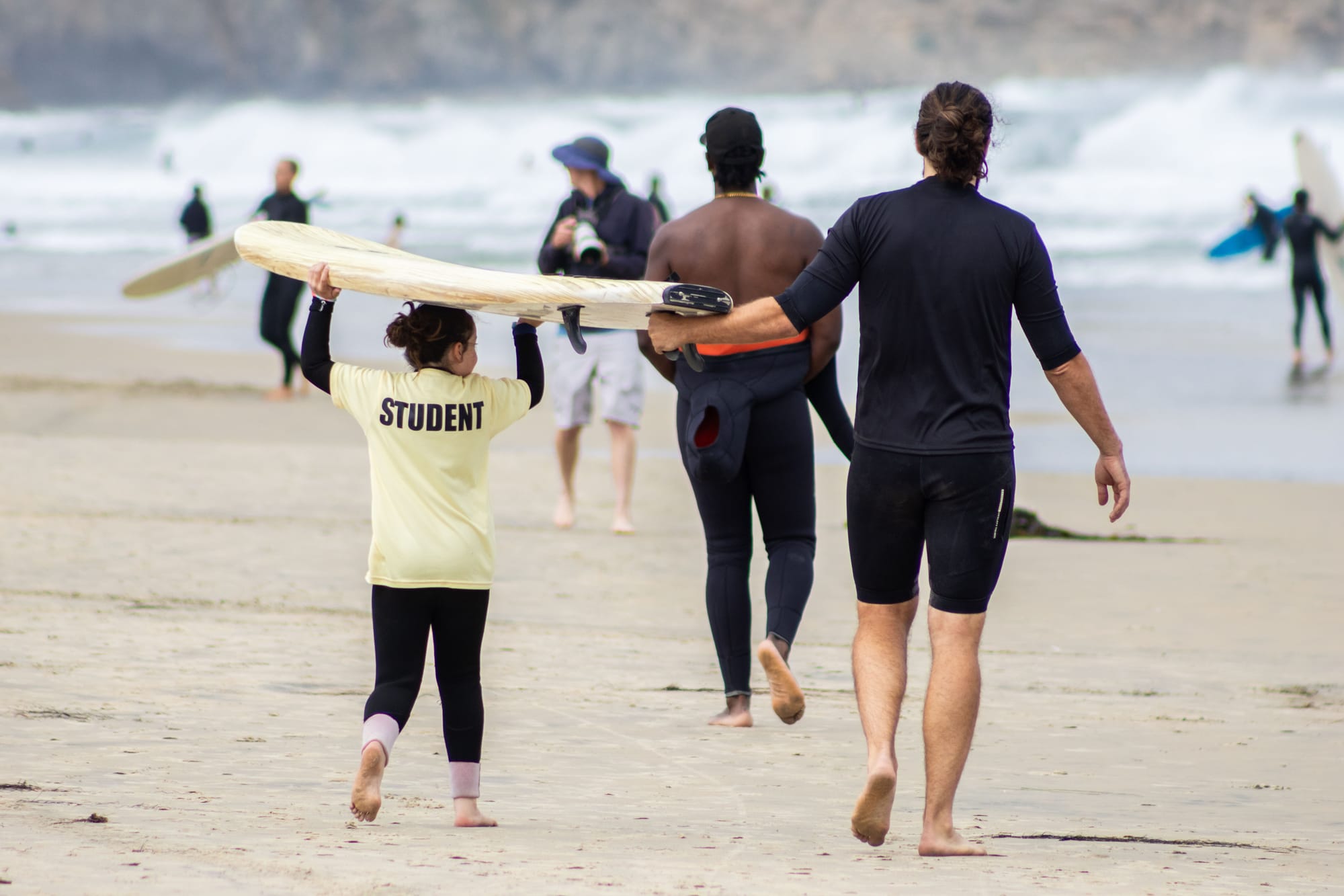 A student and some instructors walk out to the ocean with a surfboard