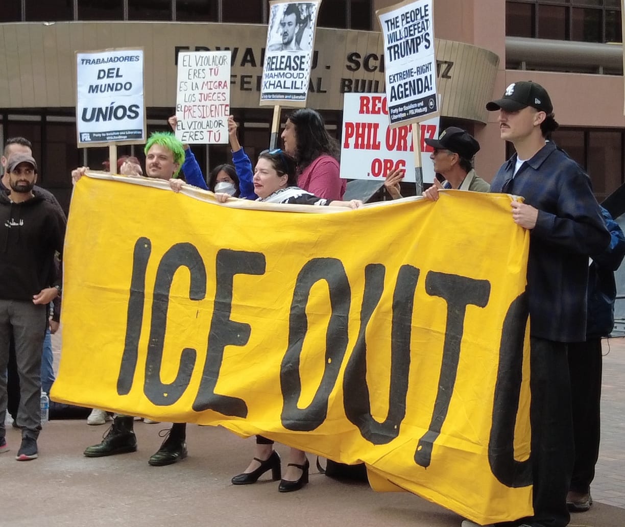 people protest outside holding a banner that reads ICE OUT