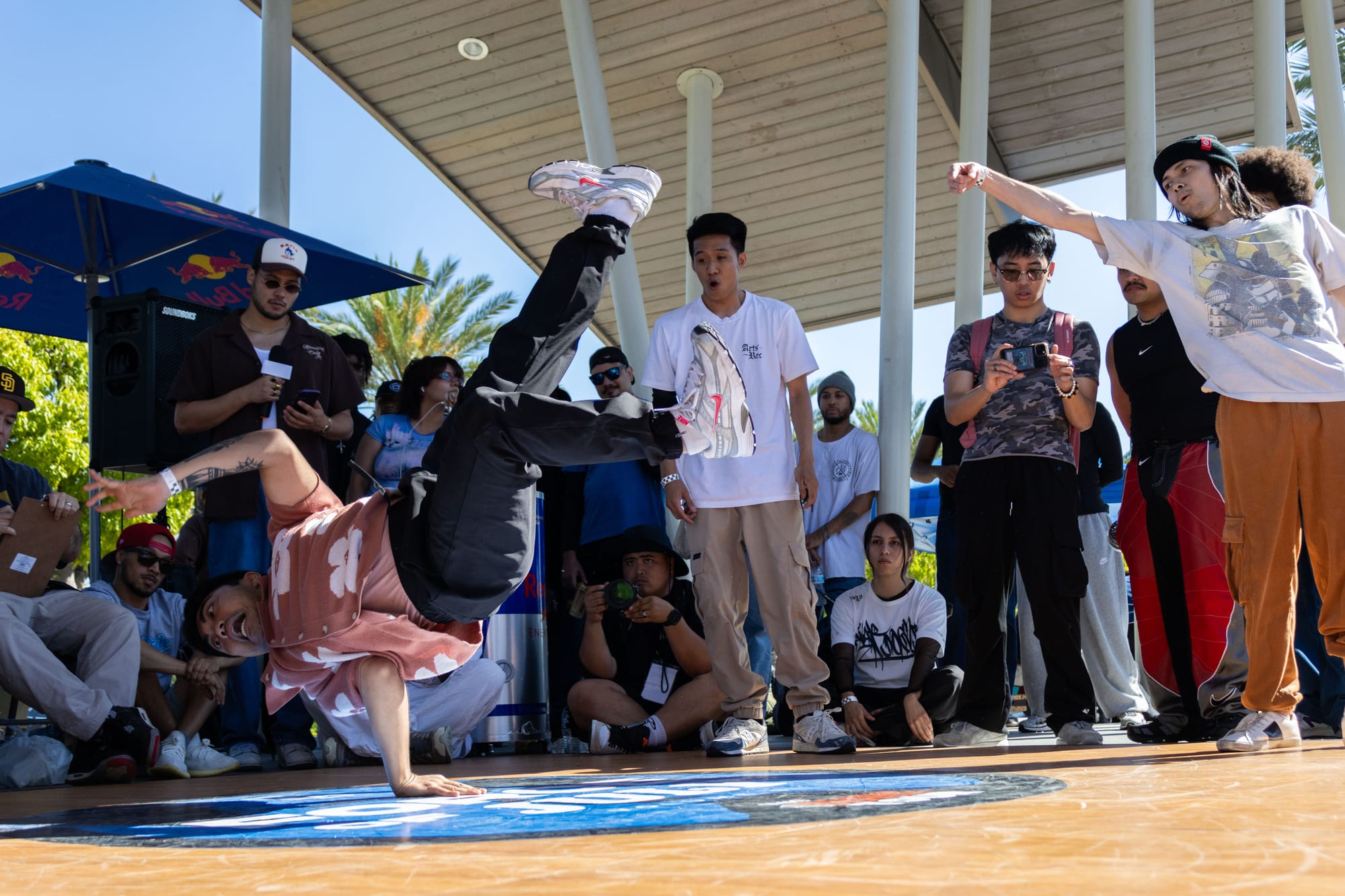 A dancer performs in a breaking competition in a crowd outside in a park.
