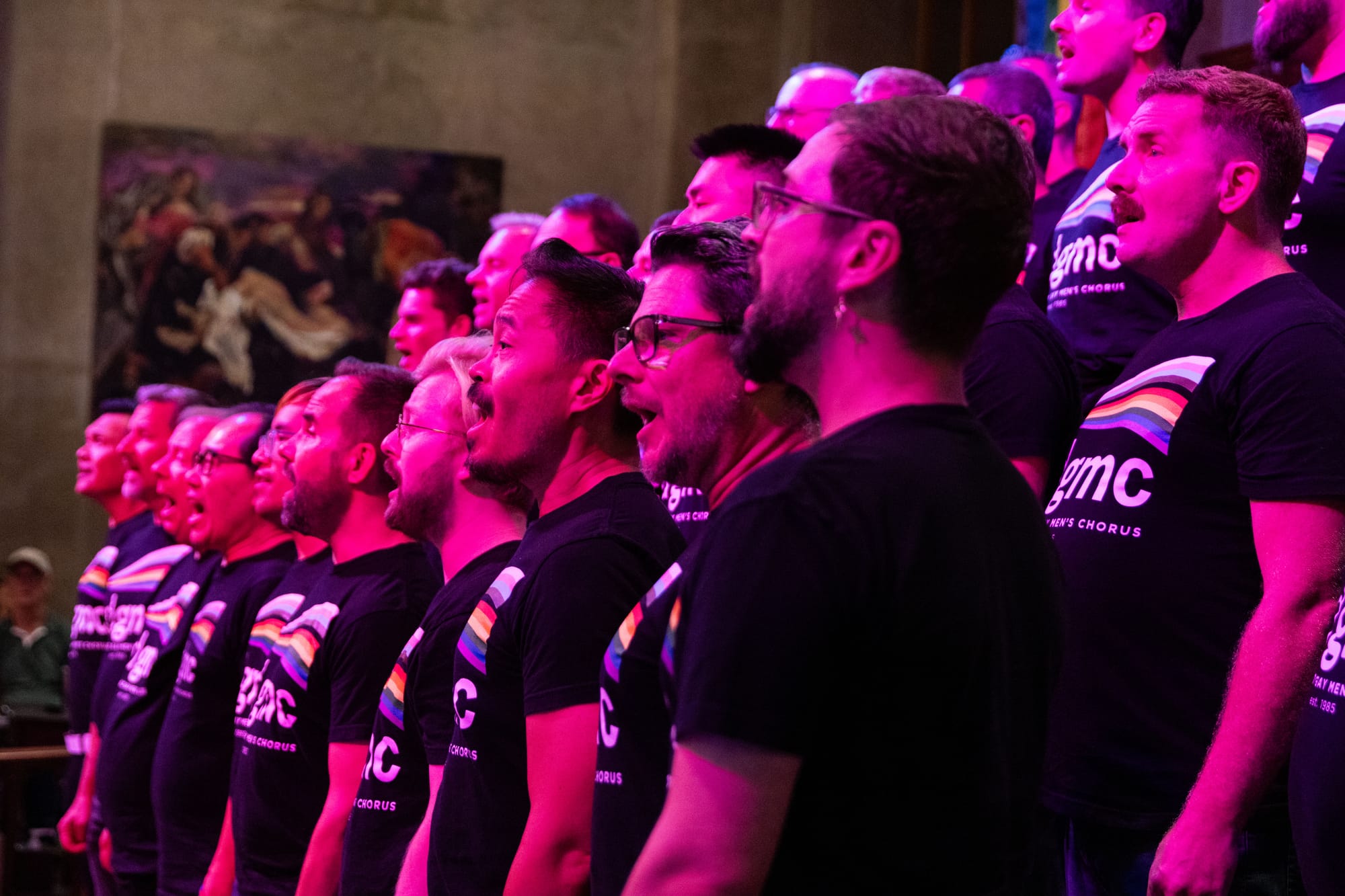 A group of men in black t-shirts with pride flags on them sings in a church