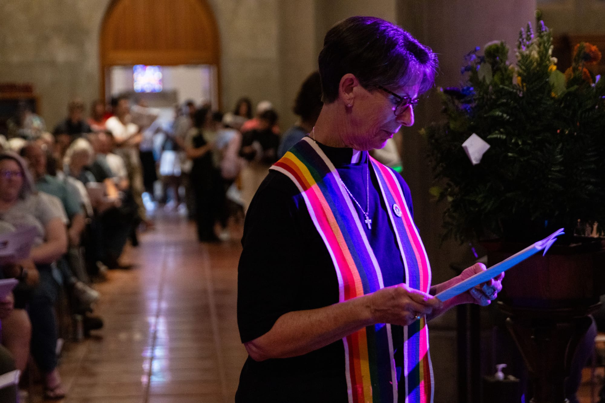 A pastor with a rainbow stole stands in a church
