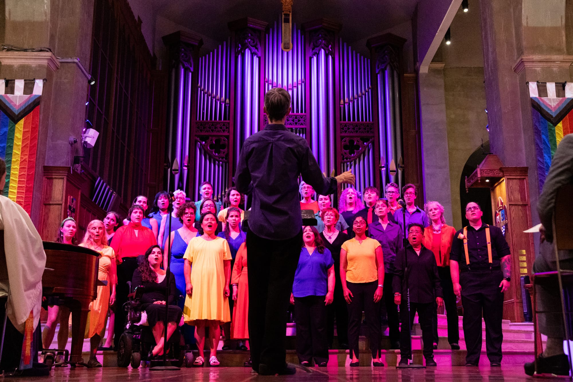 A group of women in rainbow clothing sings in front of an organ at a church.