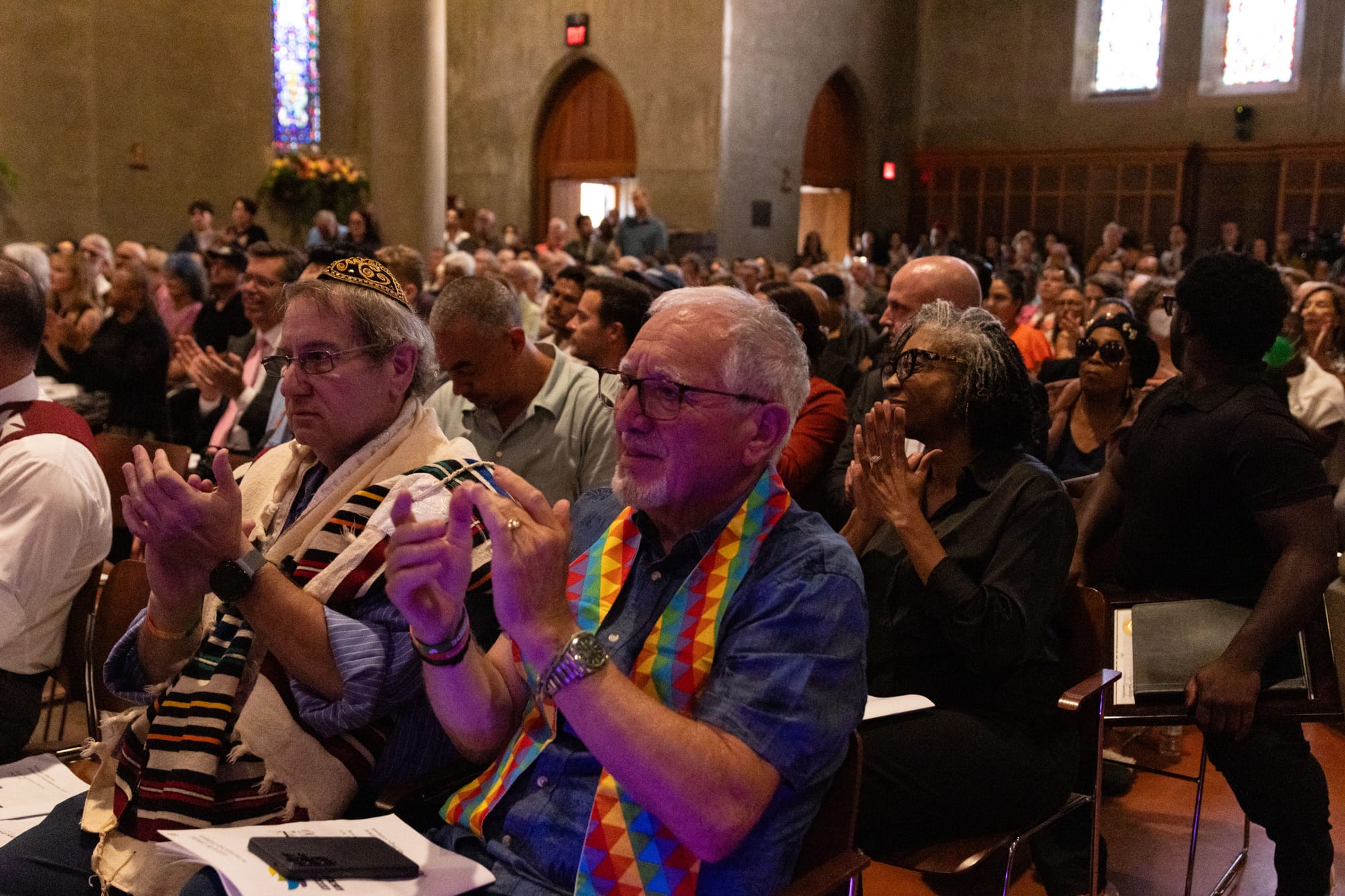 A crowd of people clap while sitting in pews at a church 