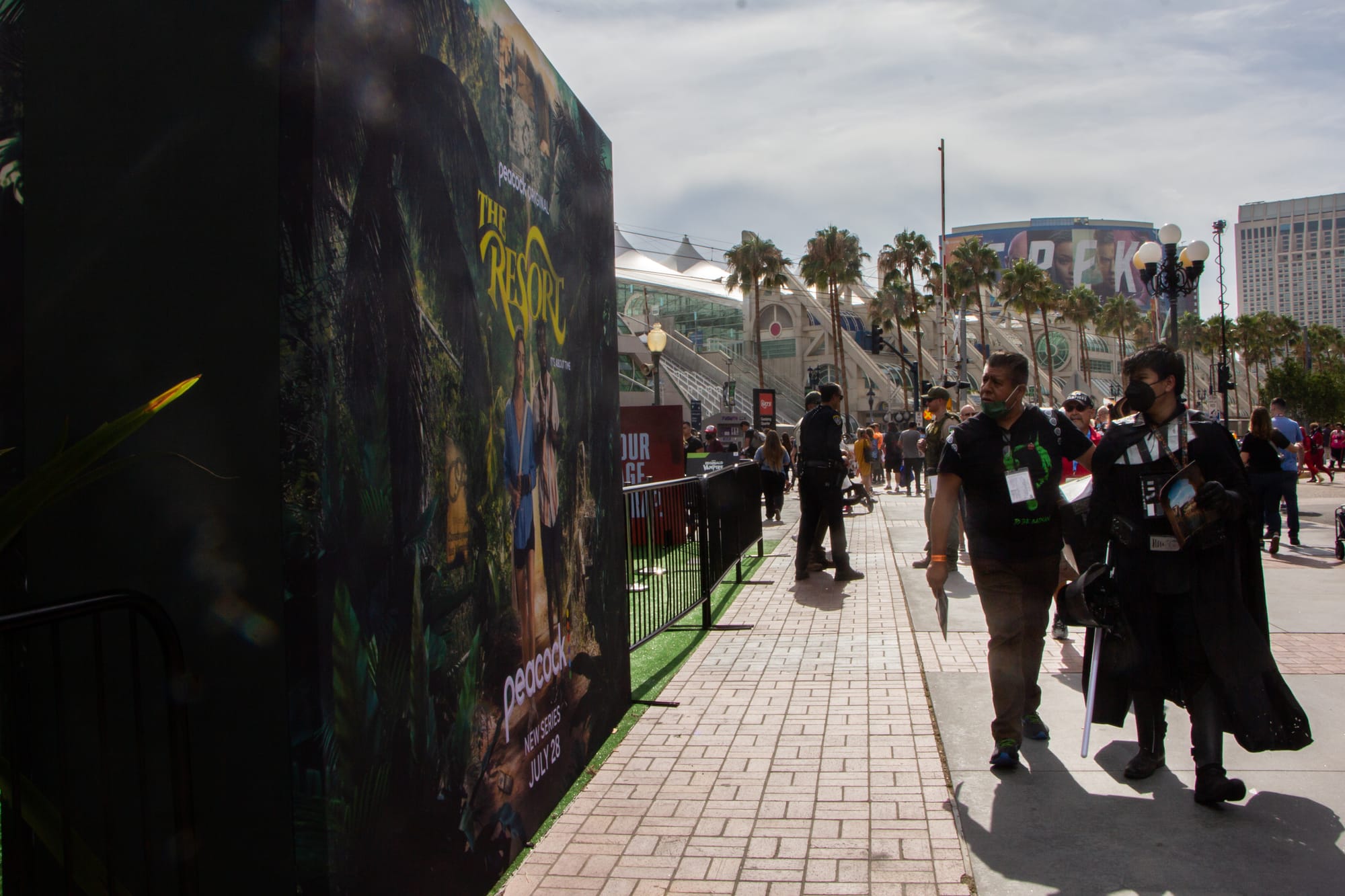 People walk outside in front of a movie poster
