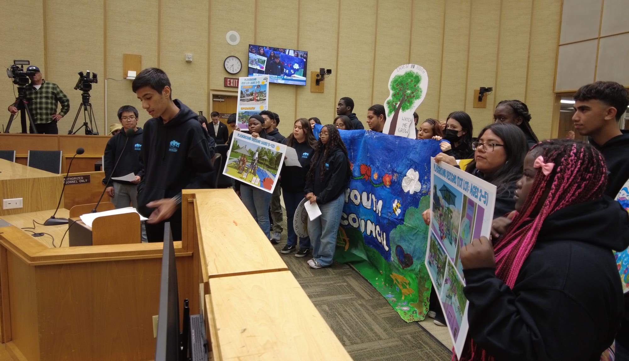 Side view of young people standing in a council room, holding up signs and banner