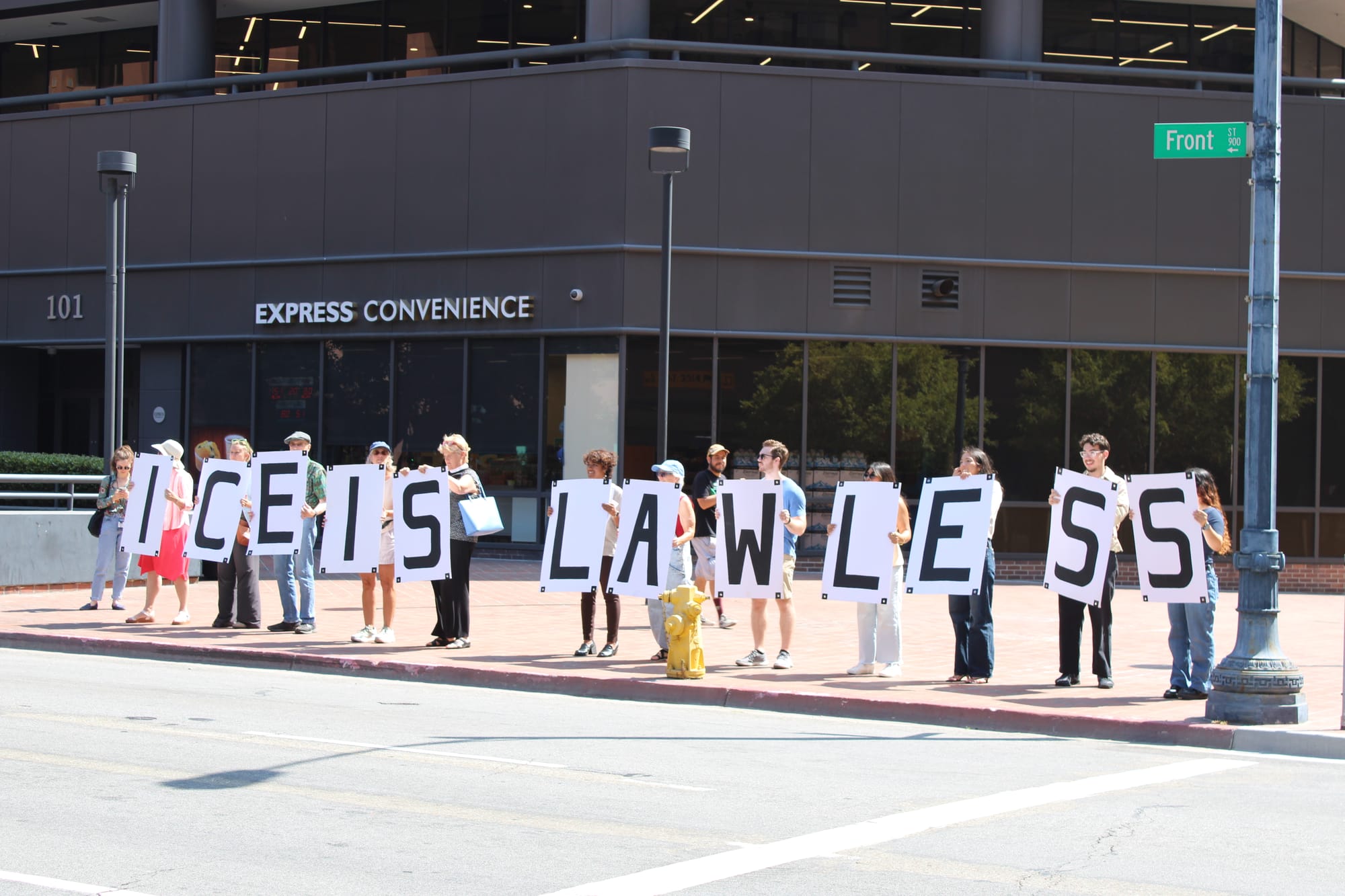 Demonstrators stand in a line outside holding letter signs that altogether read “ICE IS LAWLESS” 