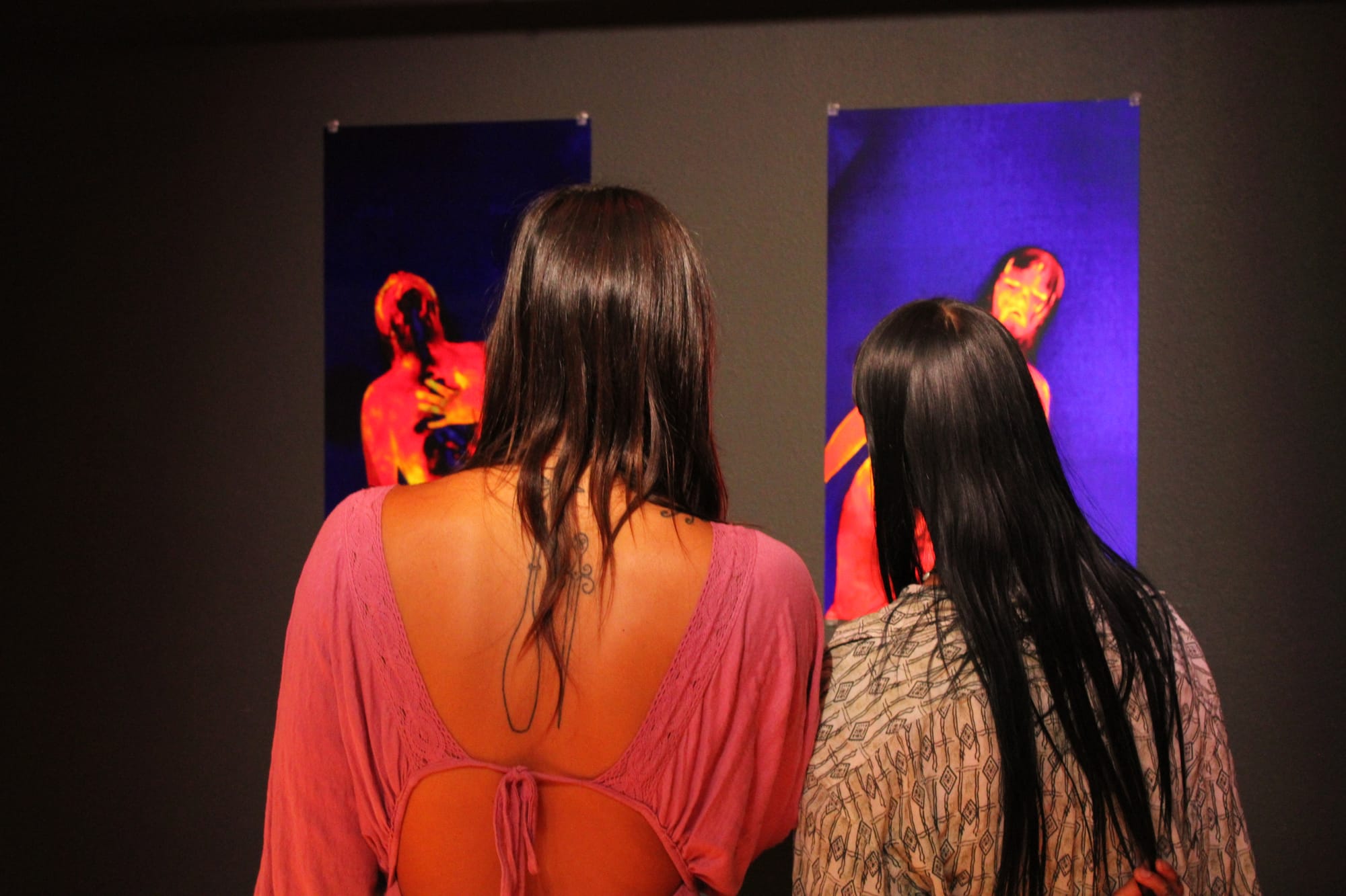 Two people view art hung on a gallery wall