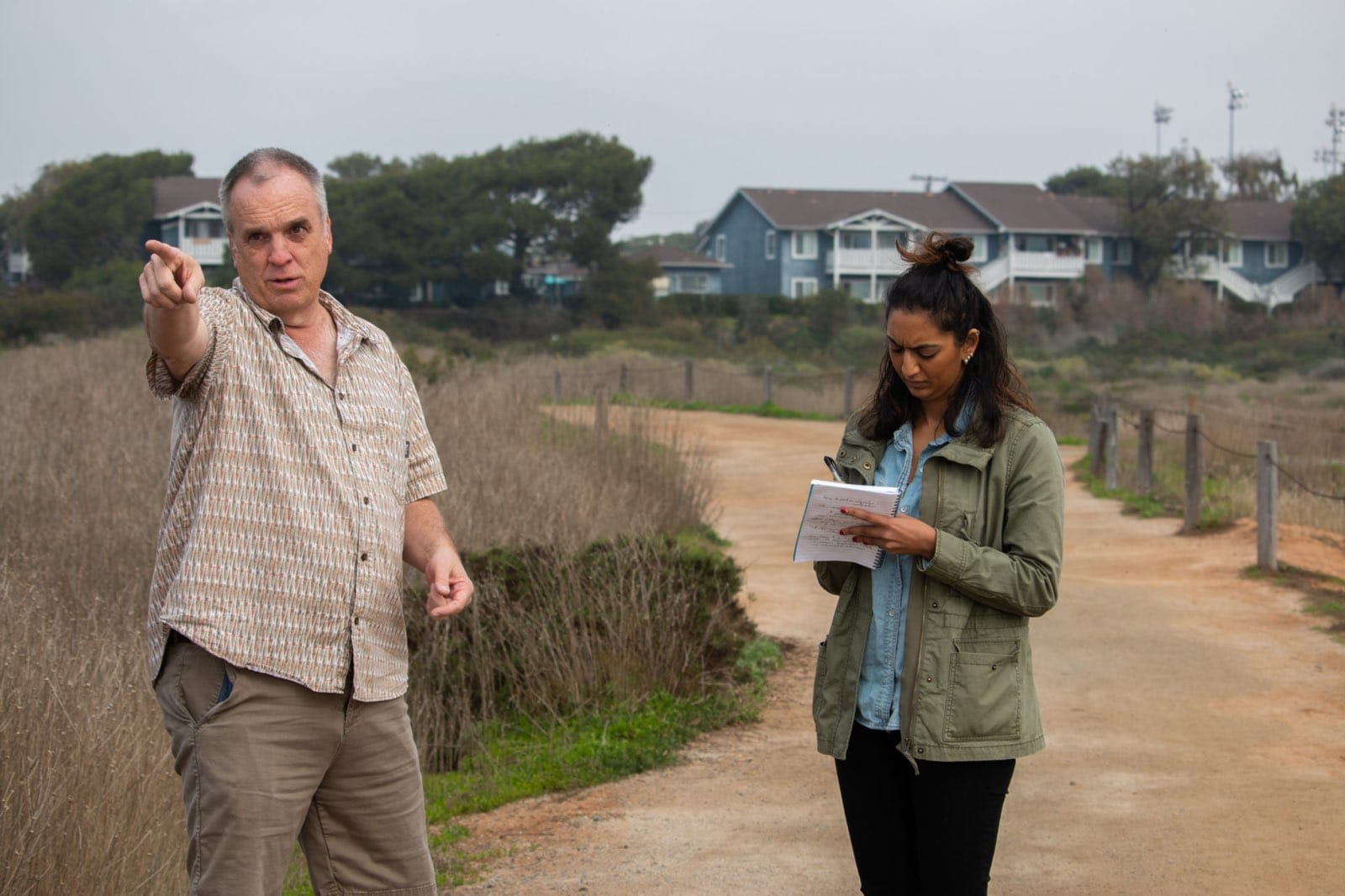 A reporter takes notes as a person talks outside in an estuary