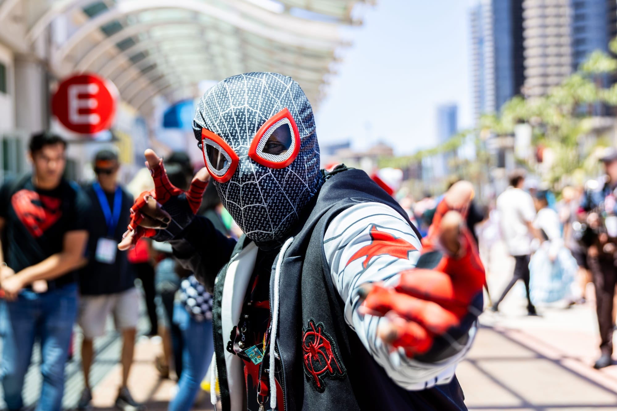A person dressed in a spider-man costume poses outside of a convention center with people in the background