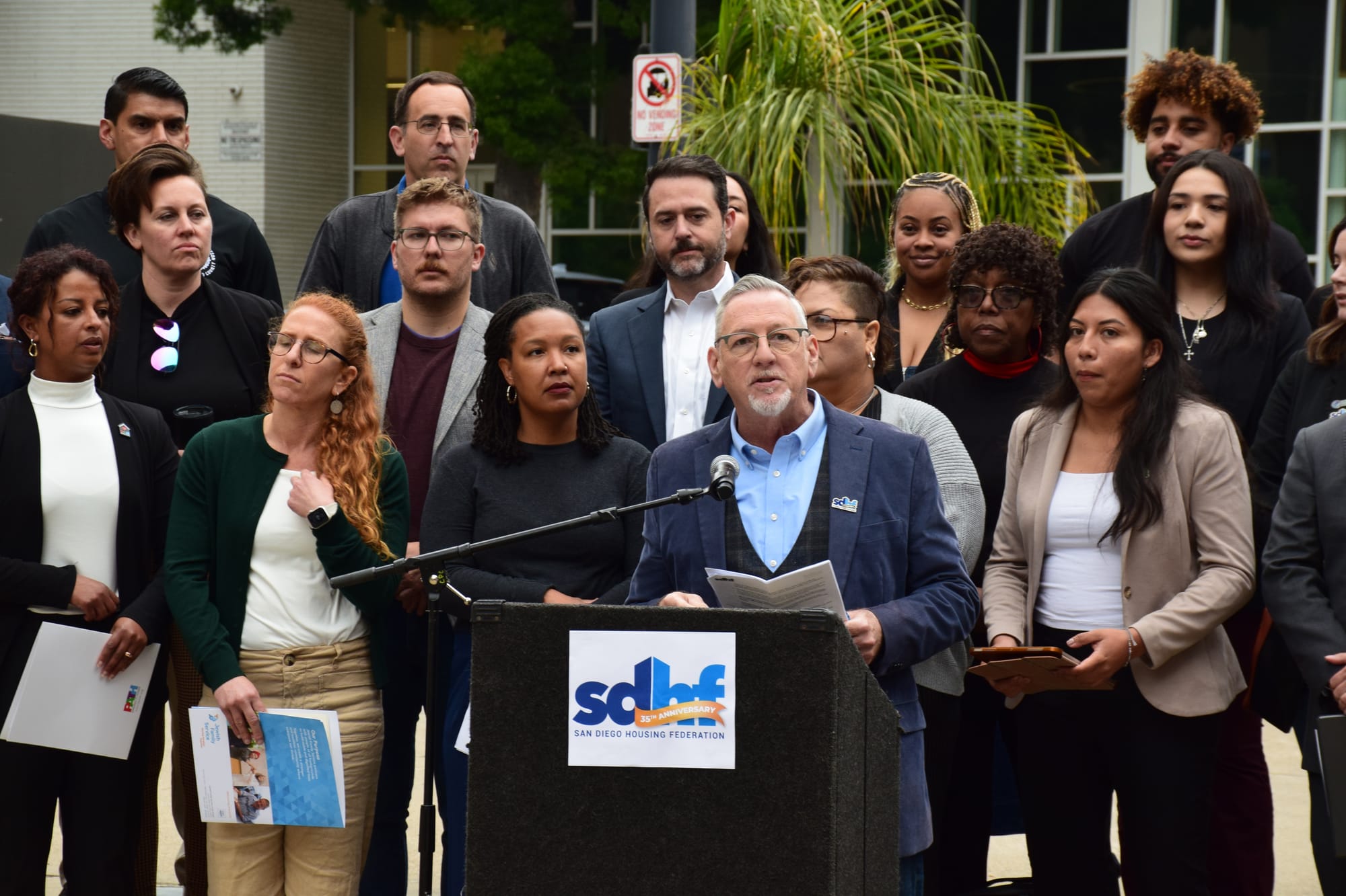 A person speaks at a podium surrounded by other people