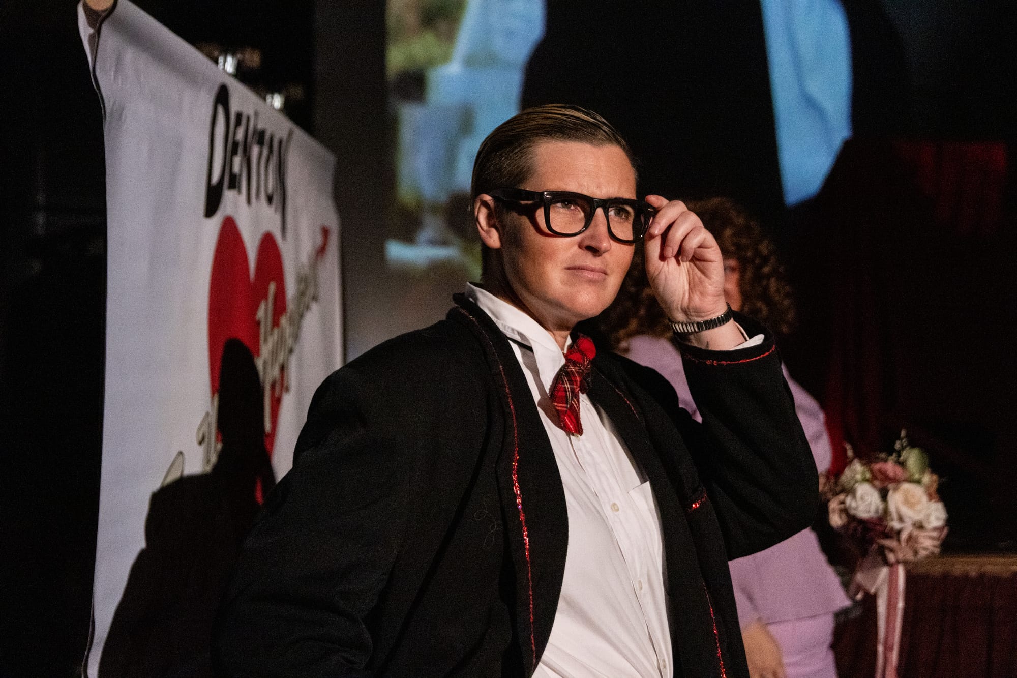 An wearing a suit actor adjusts their glasses