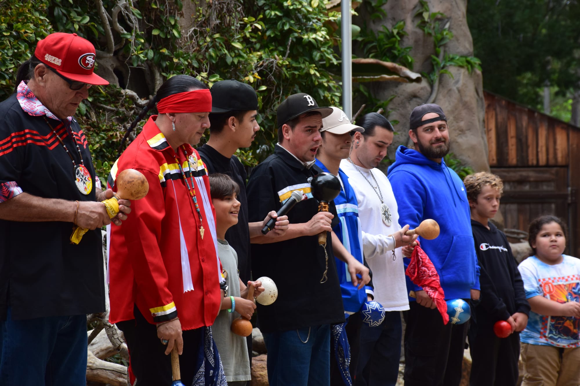 People in ribbon shirts shake gourd rattles and sing