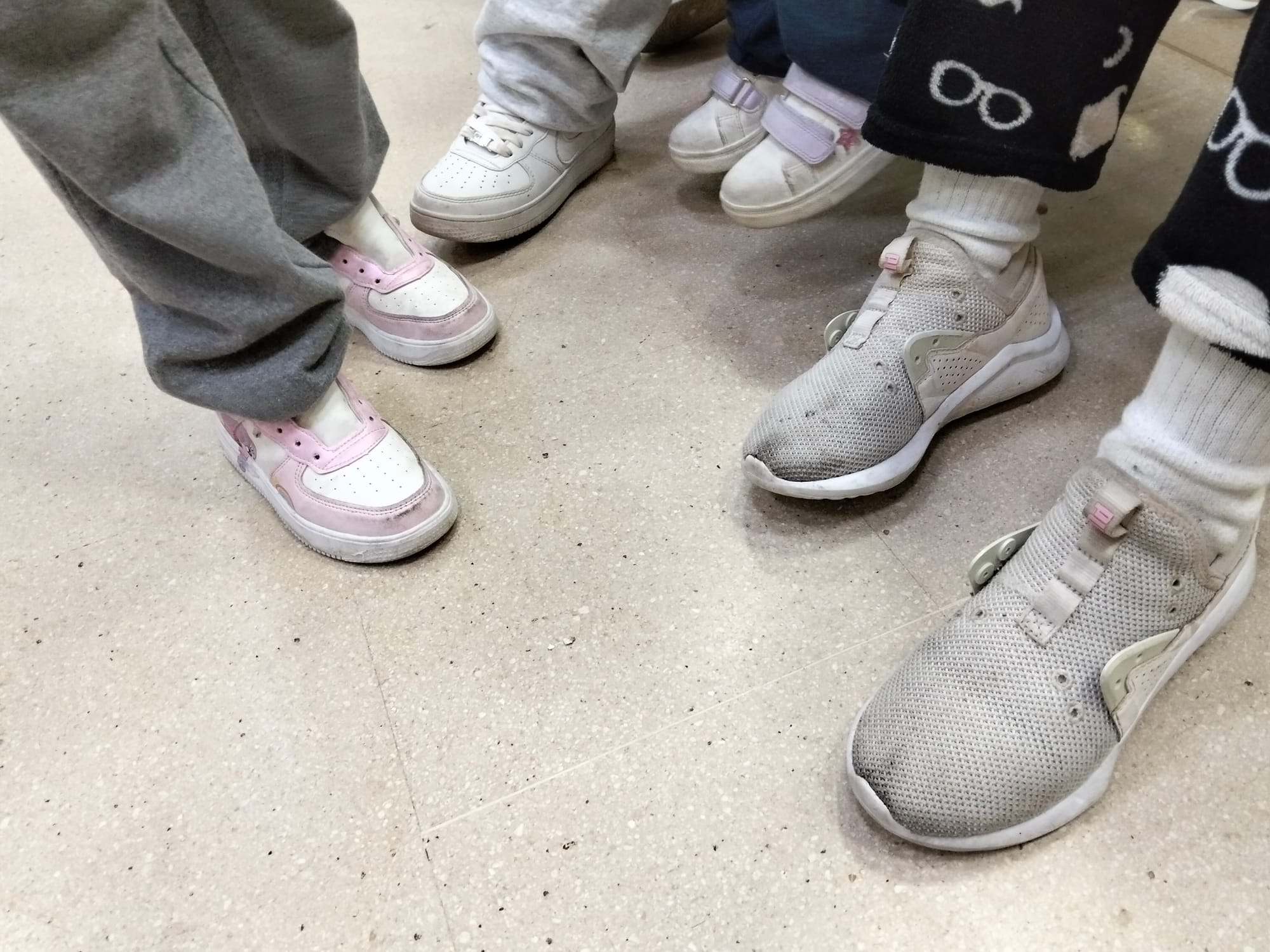 A closeup of people wearing several dirty white sneakers missing their shoelaces