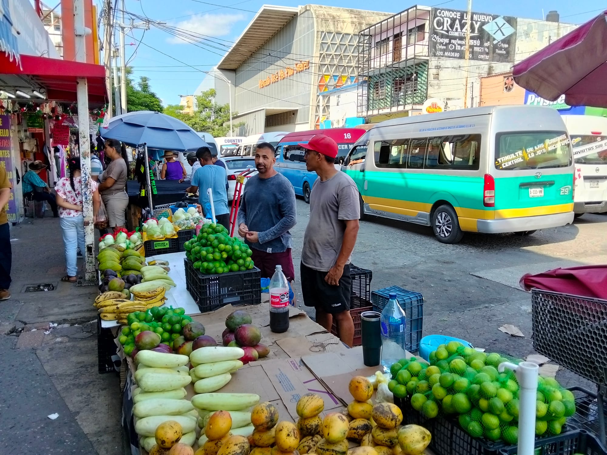 Two men stand by a table of fruit at a market in the street