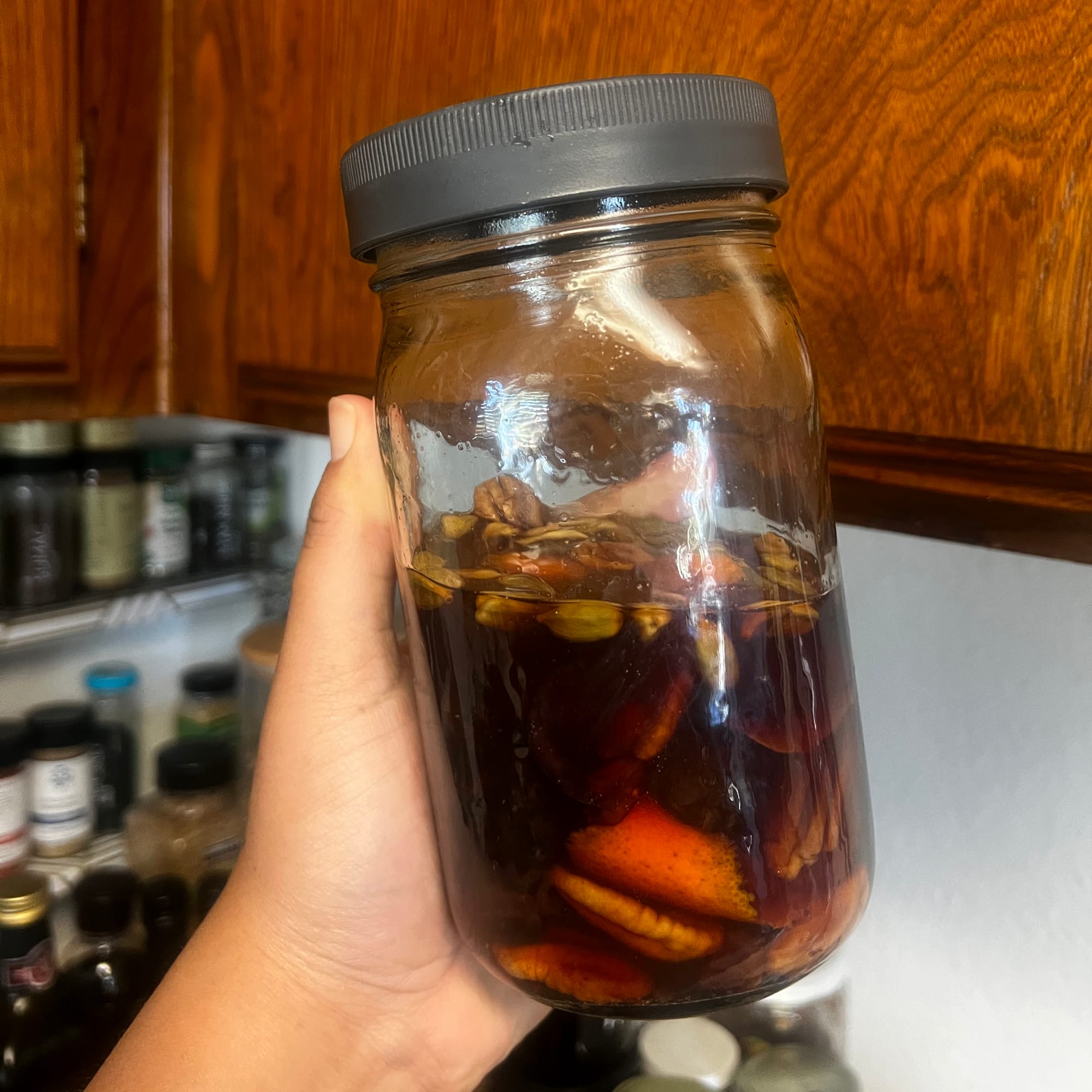 Picture of a jar with bourbon in it, as well as orange peels, pecans, cardamom pods, dried fruit, and cinnamon