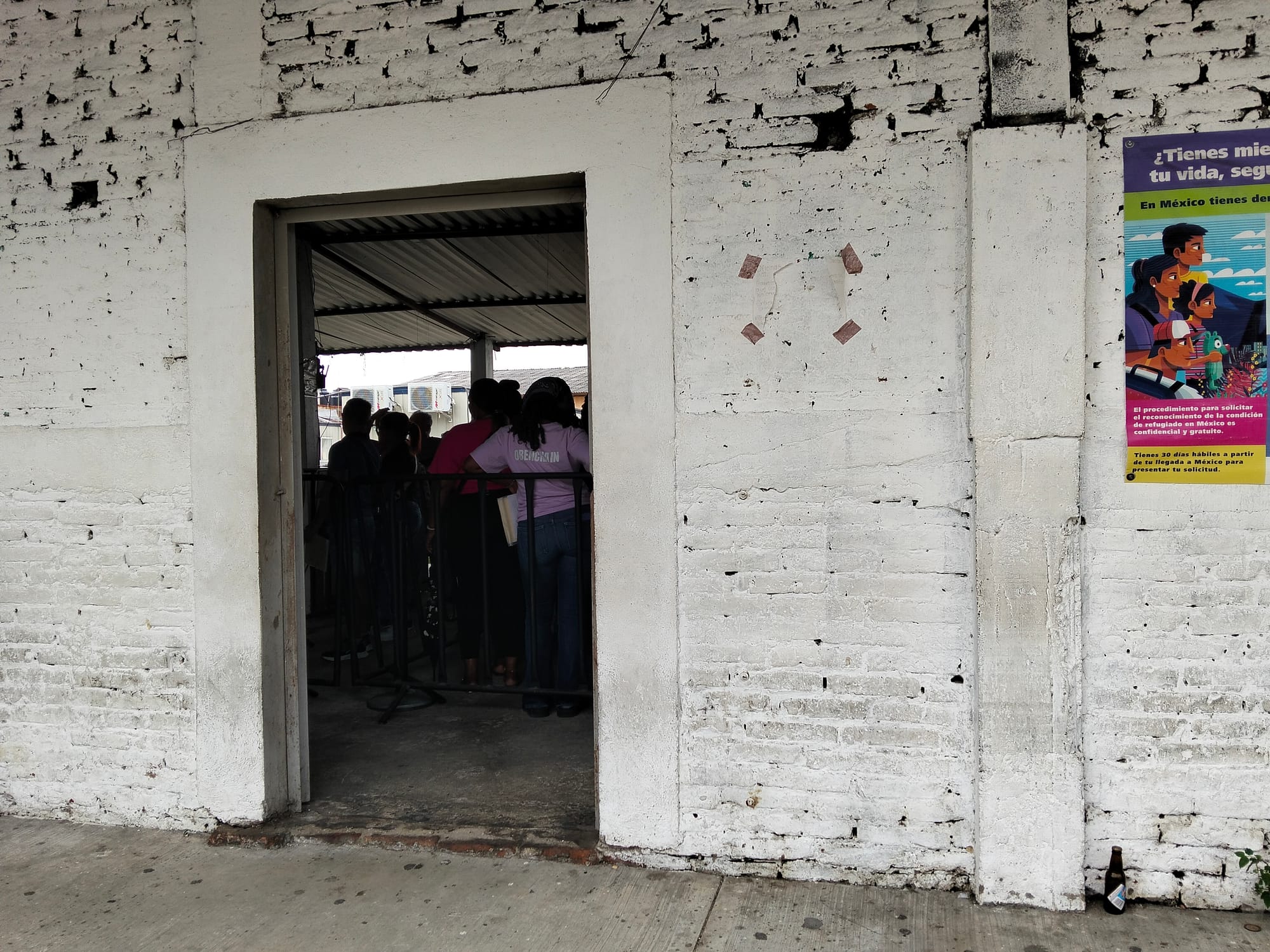 A doorway in a white brick building reveals the silhouettes of people standing in line