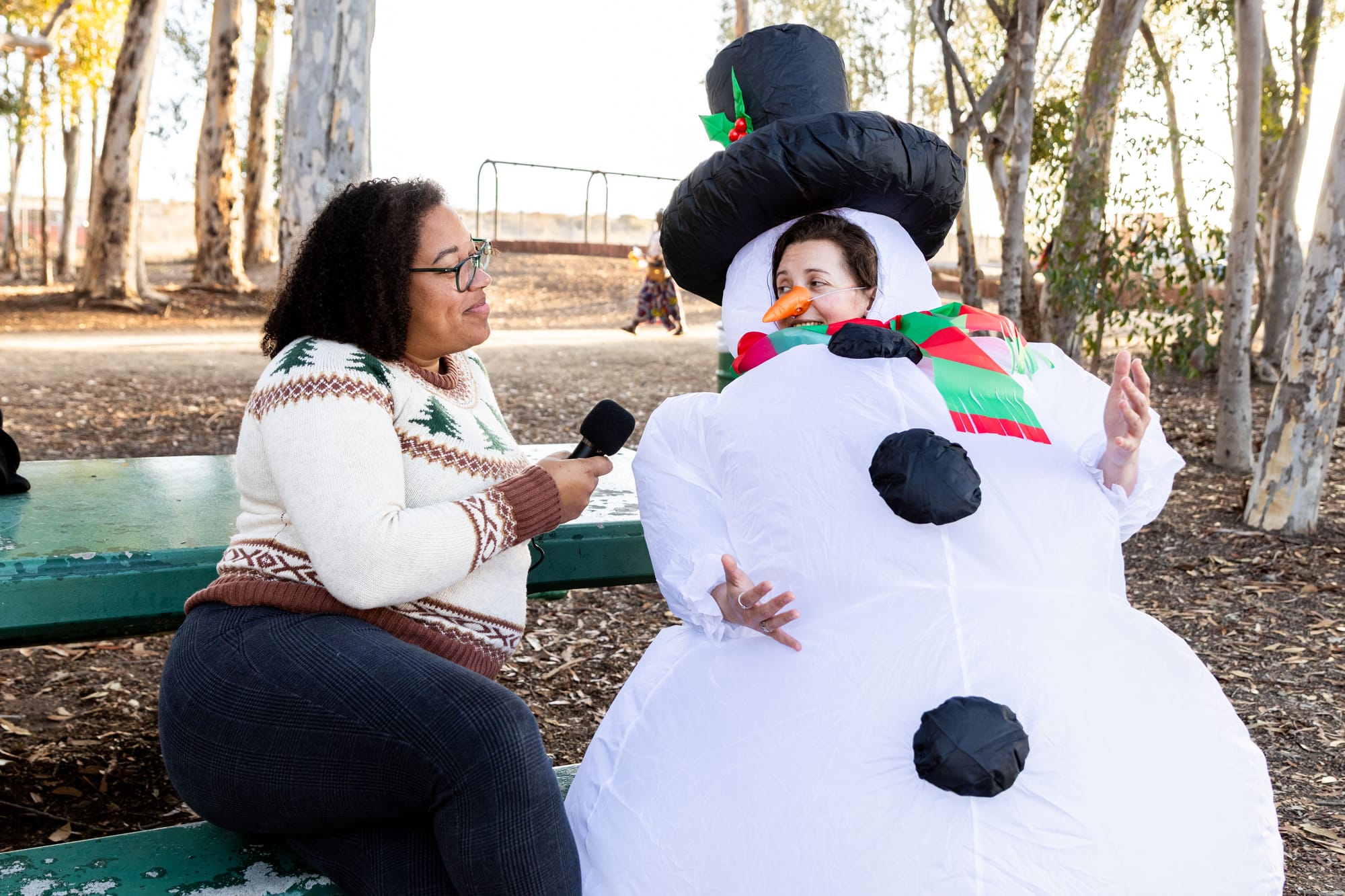 A person holds a microphone interviewing someone dressed in a snowperson costume.