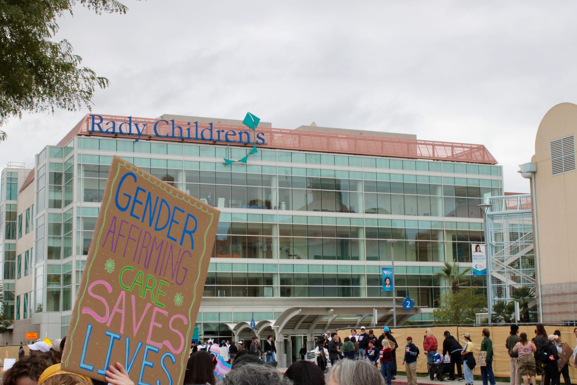 Someone holds a sign that reads "gender affirming care saves lives" outside Rady Children's Hospital during a protest.