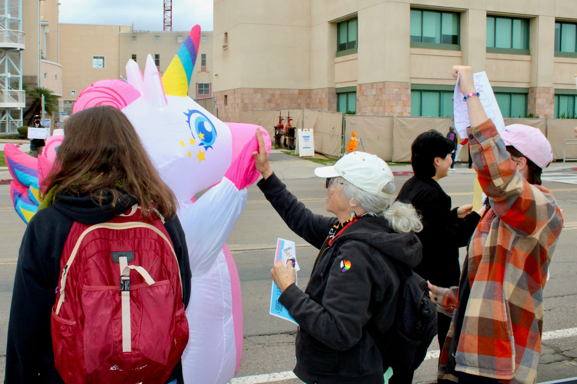 A person in a unicorn costume high fives people at a protest outside a hospital
