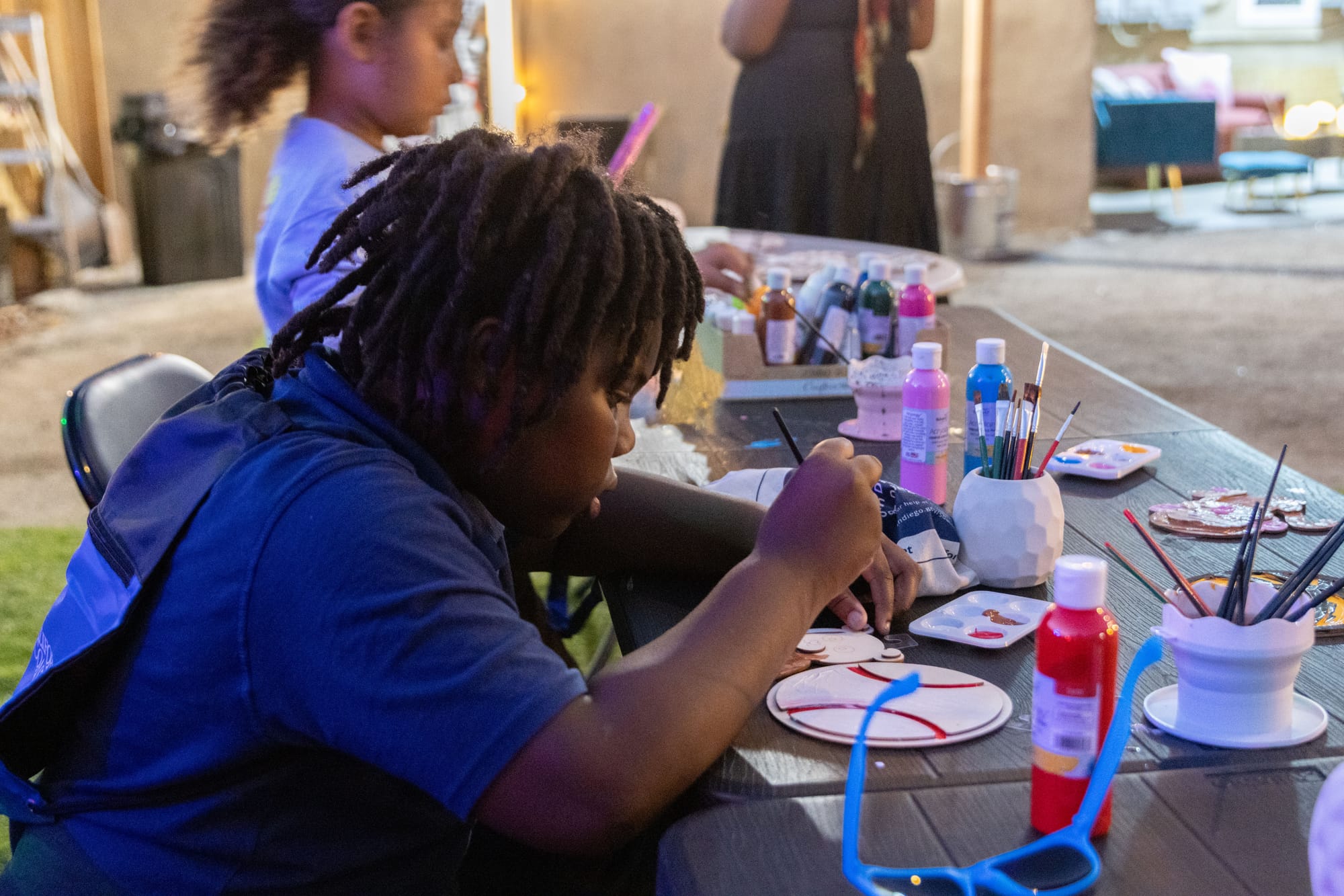 Two kids paint while sitting at a table outside.