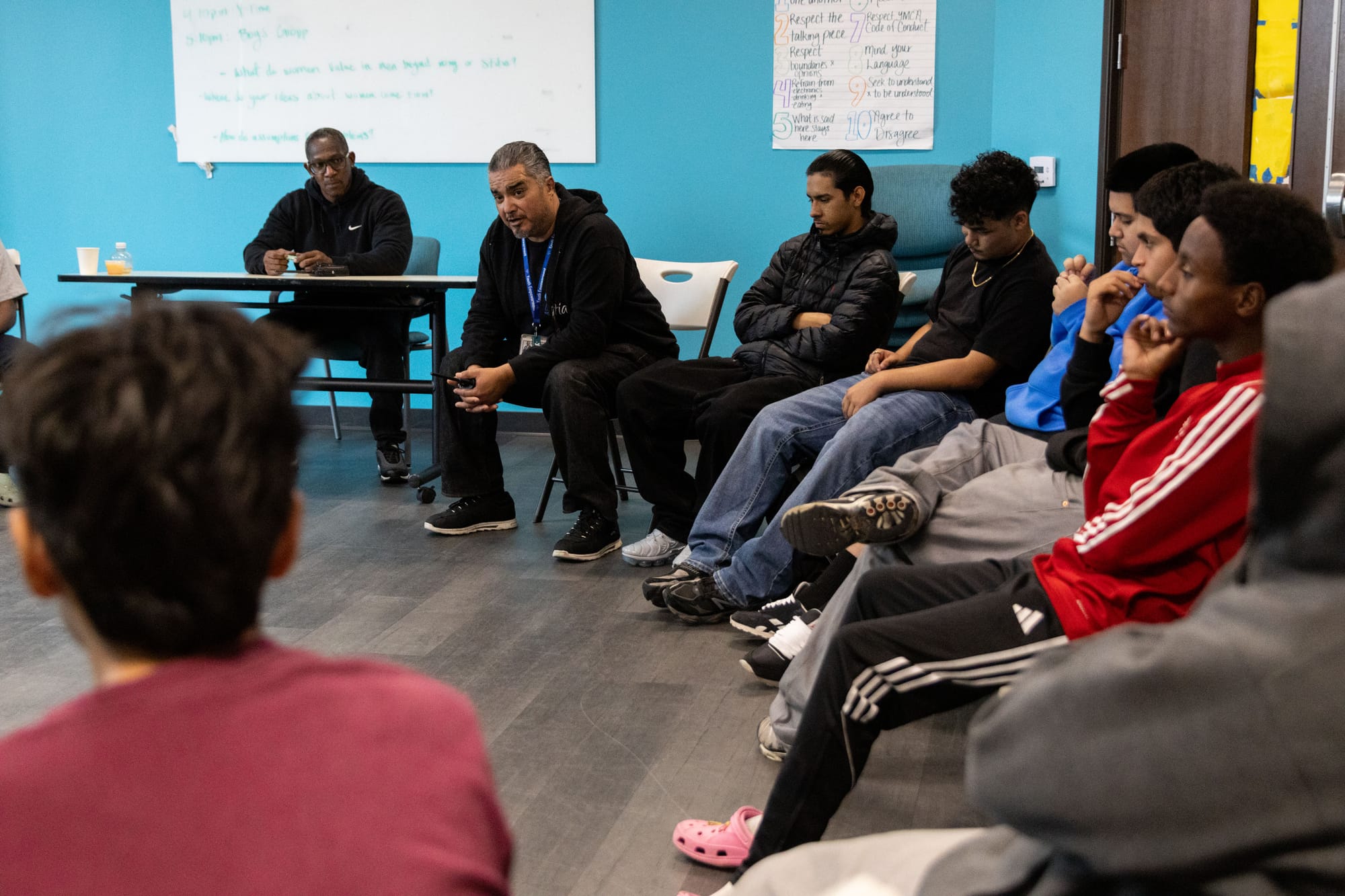 Teens and adults sit in a circle talking.