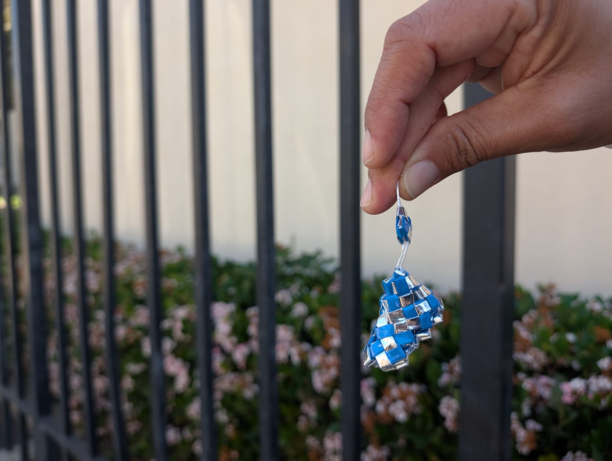 A hand holds up a blue and silver keychain-sized woven sneaker