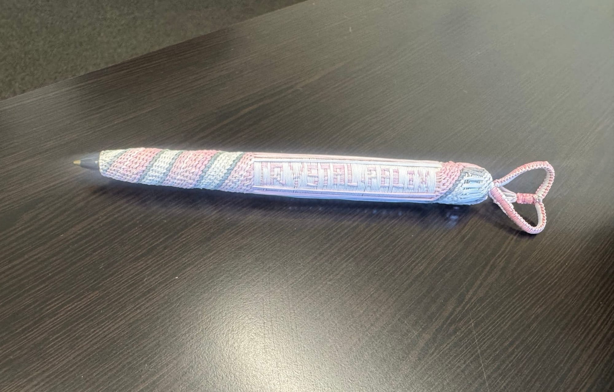 A pink, gray and white weaving spelling the name Crystal Felix covers a pen