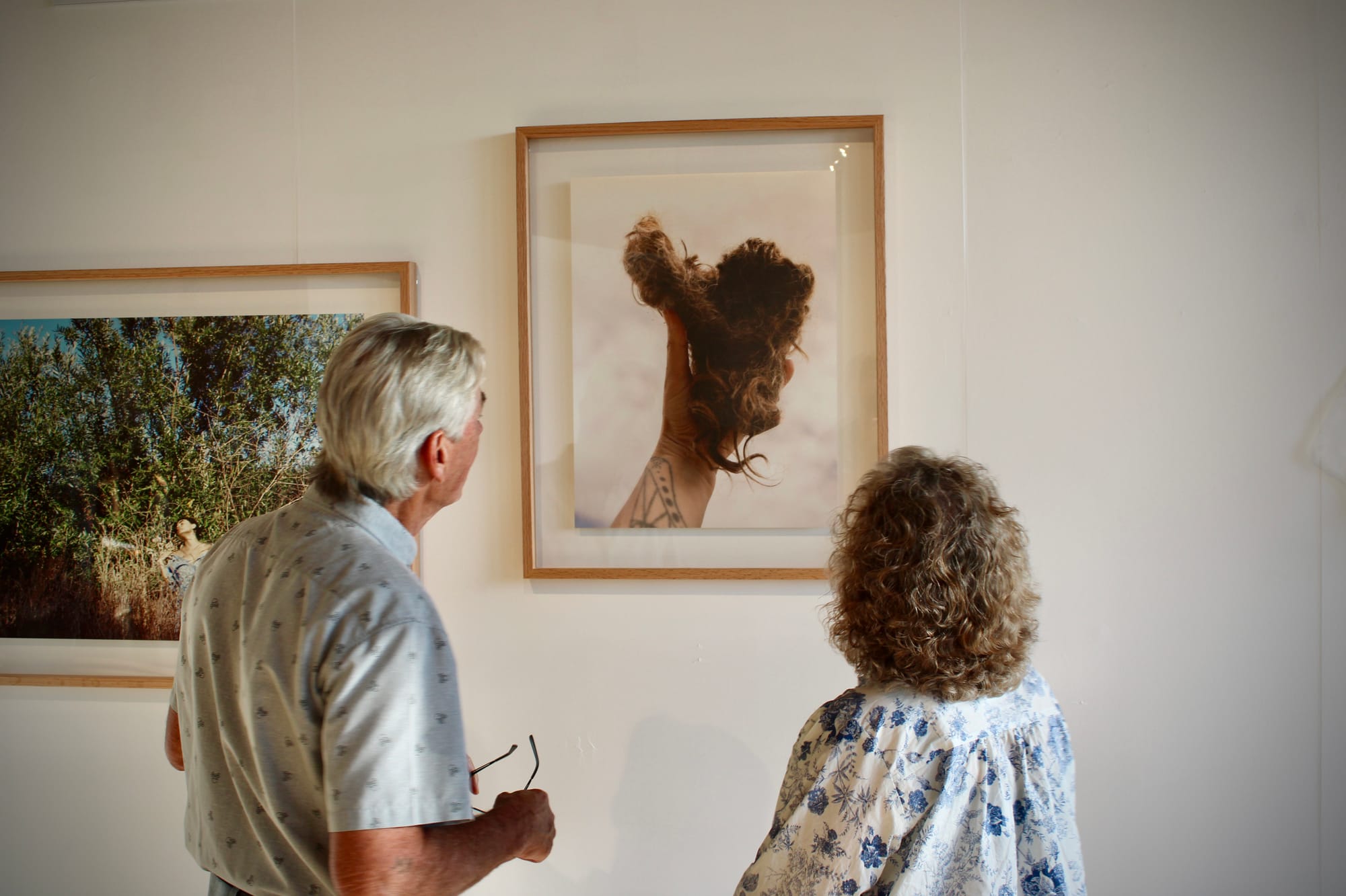 Two people observe a picture in a frame on a white wall of a hand holding loose hair.