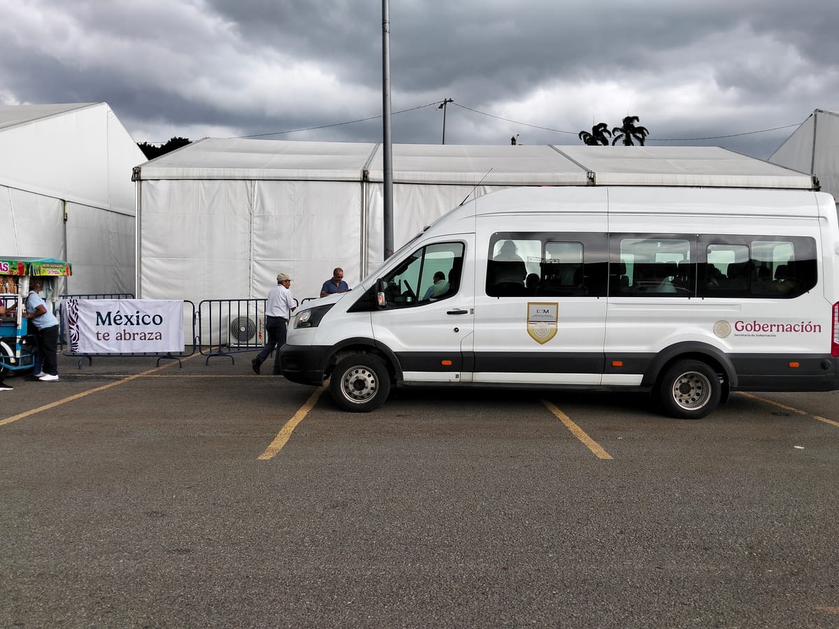 A white van with Gobernación written on the side is parked in front of a white tent with silhouettes of people leaving the van seen through the window