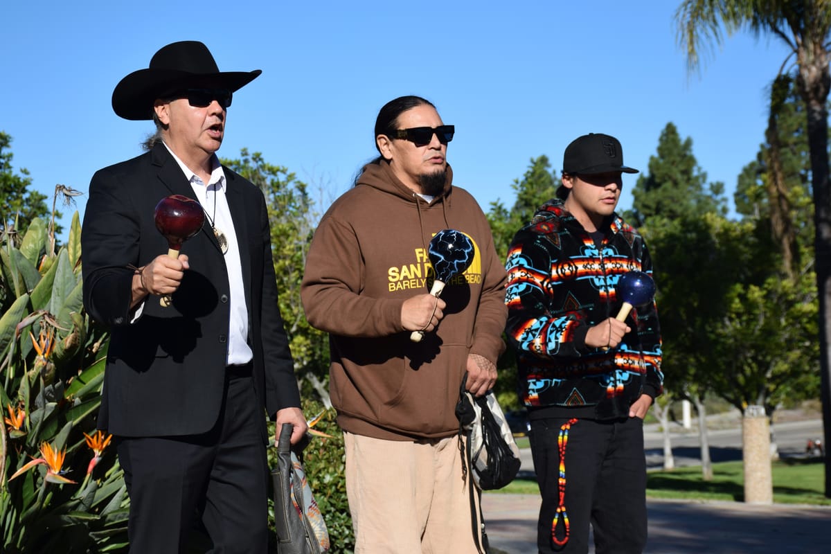 Three people shake rattles and sing outside in a park