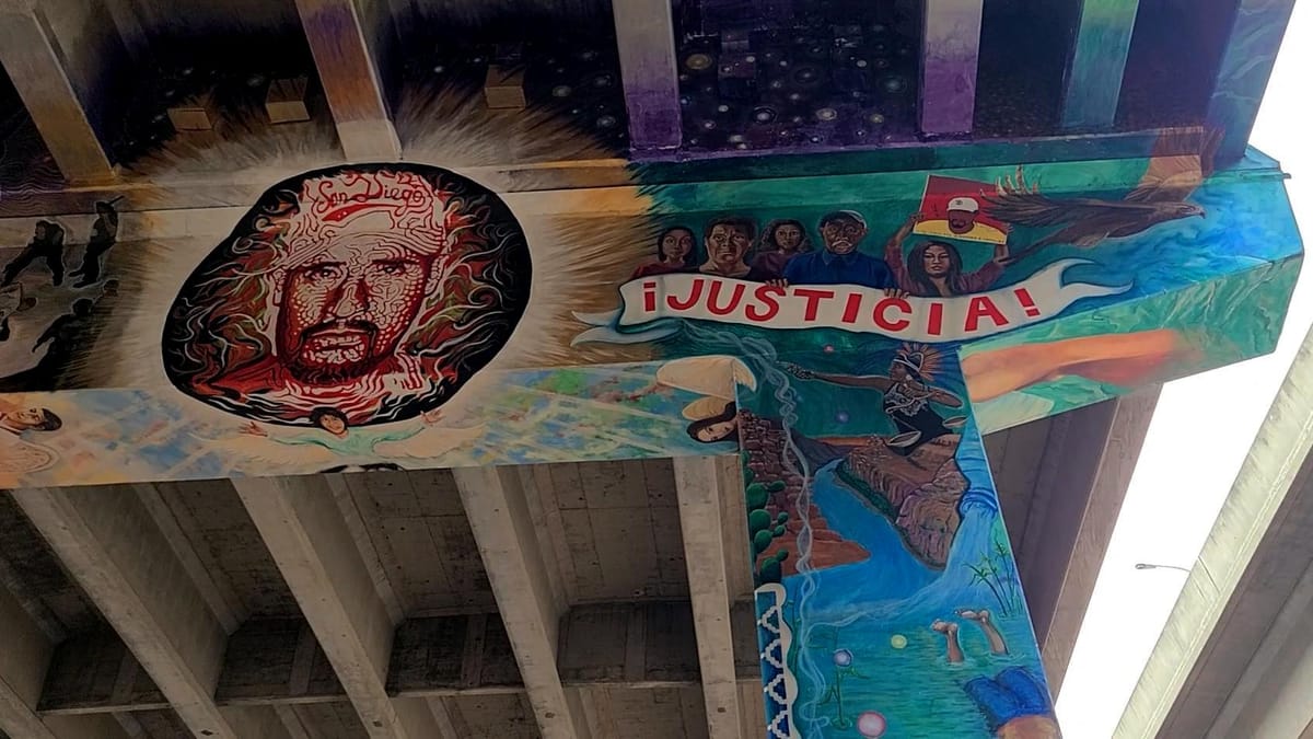 The concrete beneath a freeway bridge is painted with the face of a bearded man and the word justicia