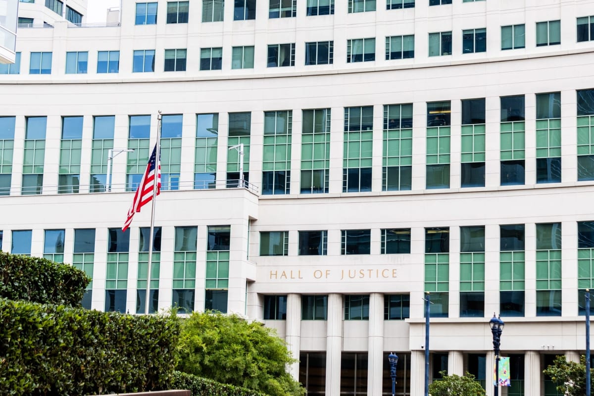 Picture of a building that says "Hall of Justice" with a bush in front of it.