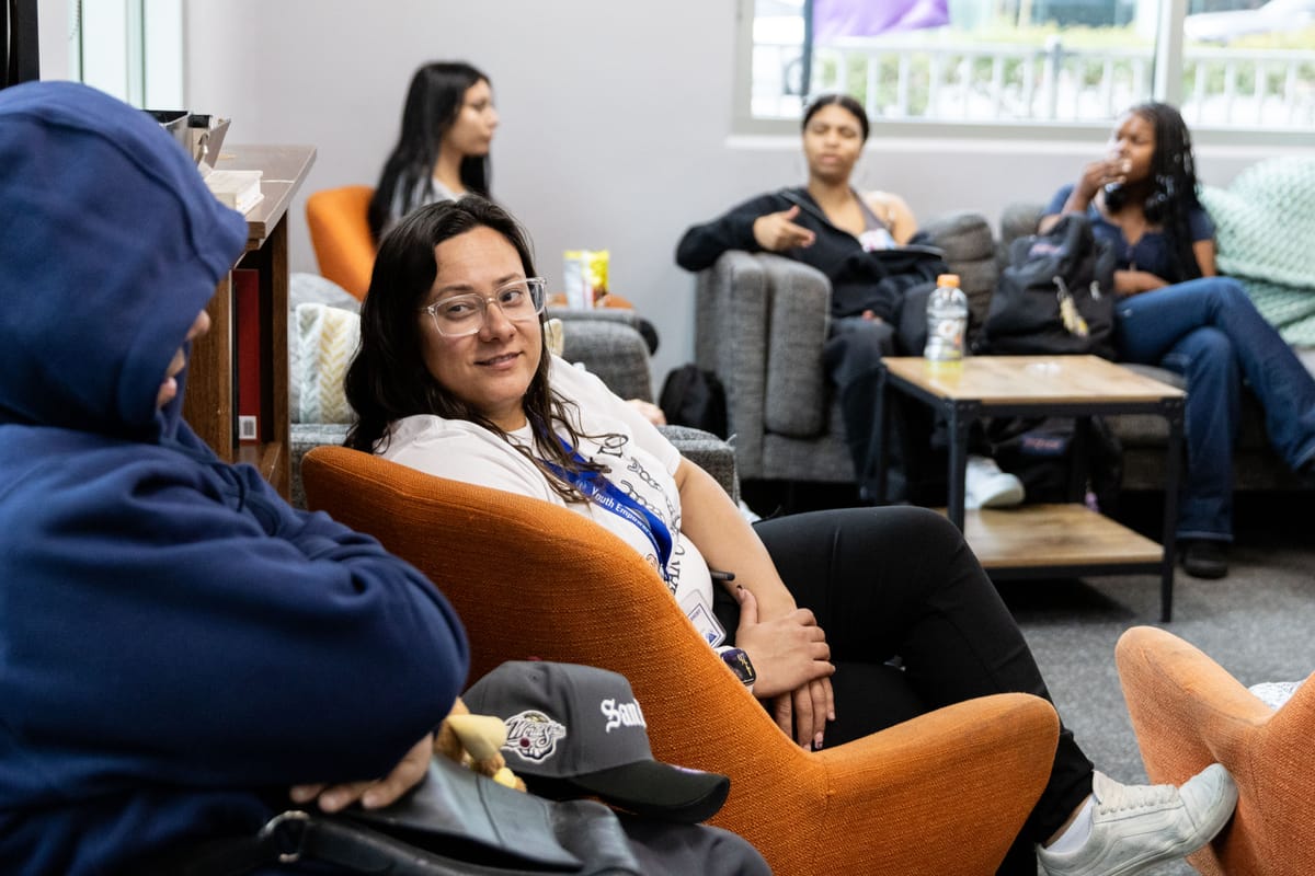 A woman sits with teenagers on chairs and sofas talking.