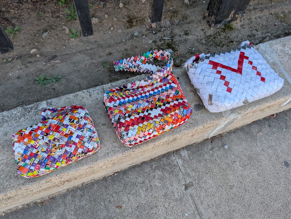 Three woven purses in several colors on a gray sidewalk