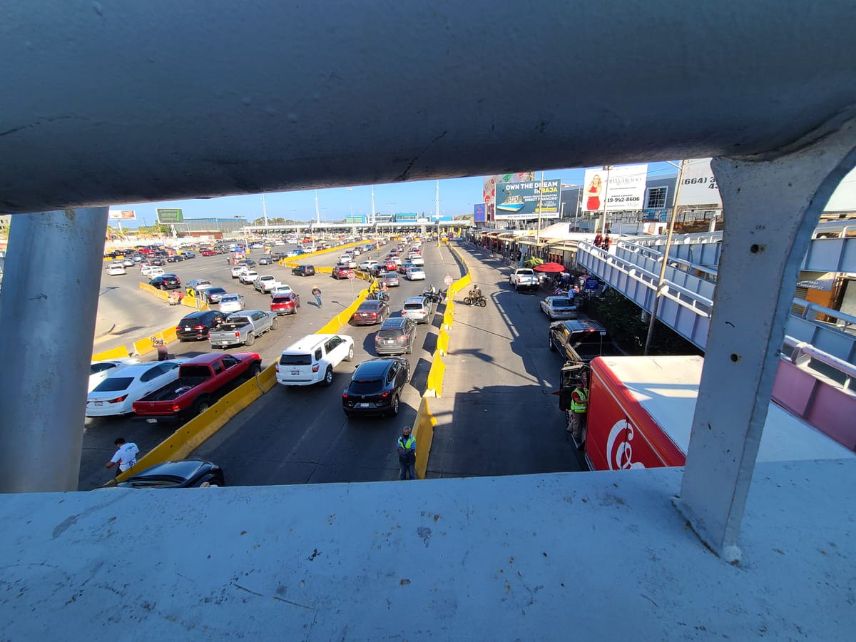 A guardrail frames a view of cars in line between low yellow walls in front of booths in the distance