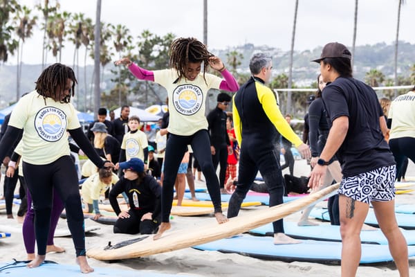 A child practices their balance on a surfboard while still on the sand