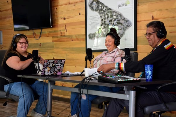 Three people sit at a table recording a podcast 