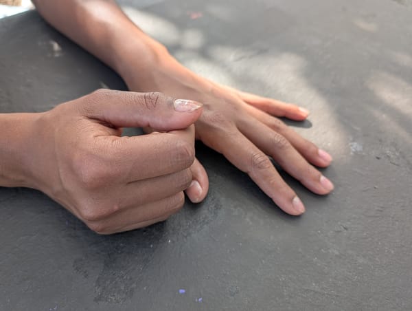 One hand lies flat on a table and the other curls with the thumb up