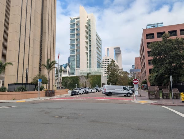 A white van is parked on the street in between tall, brown, government buildings.