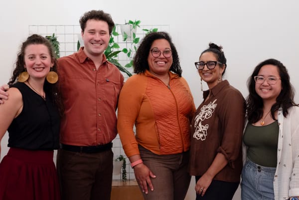 Five people in autumnal looking clothes pose for a photograph standing side by side.