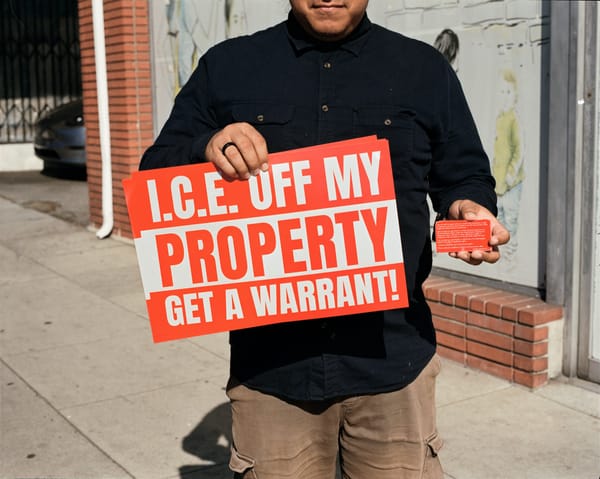 A man holds a sign that says I.C.E. off my property get a warrant! and a red card