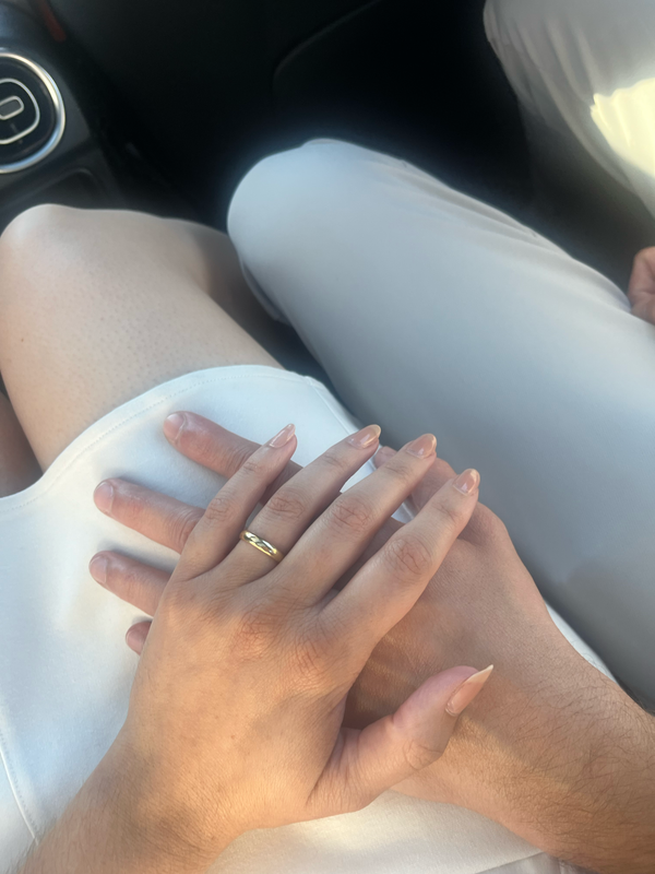 A woman's hand with a gold ring on the ring finger lies on top of a man's hand