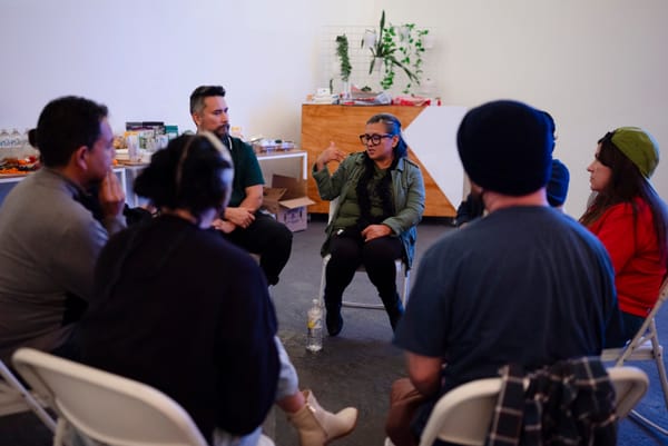 A woman speaks to a group of people sitting in chairs facing one another. 