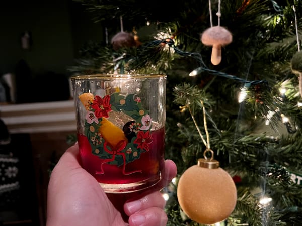Picture of a rocks glass with a wreath printed on it in front of a Christmas tree