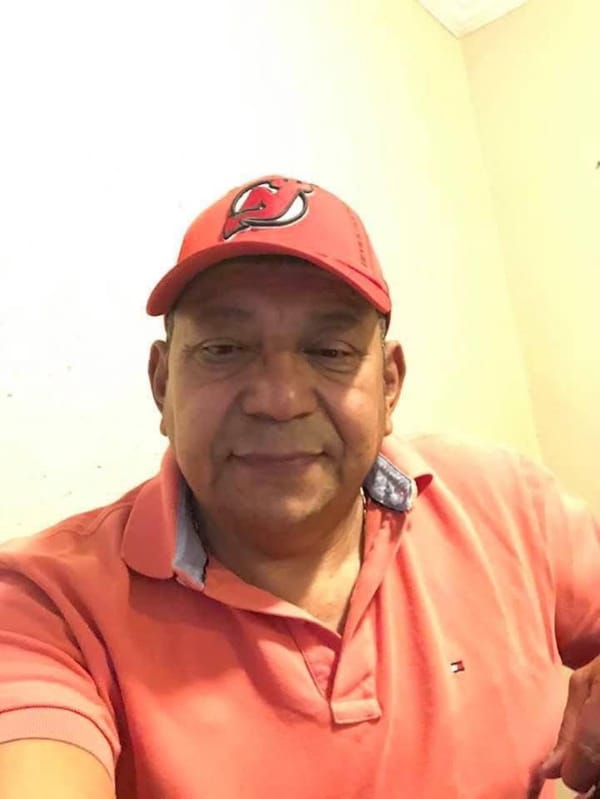 A man in an orange baseball cap and orange collared shirt looks straight at the camera for a selfie